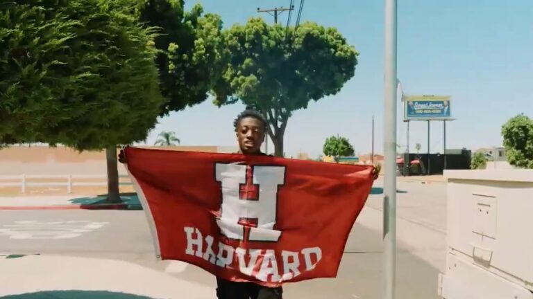 Dorian Franklin holding a red Harvard flag on a street in Southern California